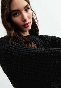 Zwarte gebreide trui met een ribbelpatroon en een ronde halslijn. De stof ziet er zacht en comfortabel uit, met lange mouwen.