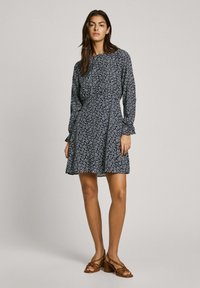 Marineblaues Blumenkleid mit langen Ärmeln, gerafften Bündchen und einem leicht ausgestellten Rock. Das Muster zeigt kleine weiße Blumen. Tragen Sie es mit braunen Absatzsandalen.