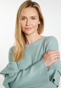 Šviesiai mėlynas dryžuotas megztinis su išplatėjusiomis rankovėmis, pasižymintis minkšta tekstūra. Apykaklė yra laivo formos, suteikianti kasdienį įvaizdį.