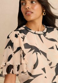 Roosa mustritega topp mustade abstraktsete kujunditega, millel on volditud lühikesed varrukad ja ümar kaelus. Sujuv ja kerge kangas.