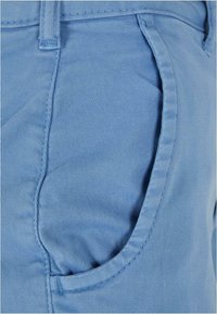 Gros plan d'un tissu bleu clair montrant la poche avant et le détail des passants de ceinture d'un pantalon.