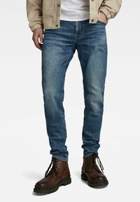 Blå denimjeans med slim fit, med urtvättade områden och klassiska sömnadsdetaljer. I kombination med bruna läderankelboots.