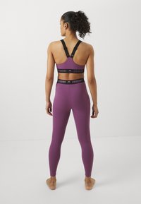 Lila edzőszett, bralette-tel és magas derekú leggings-sel. A bralette fekete pántokkal és logós derékpánttal rendelkezik. Simaság, testhezálló dizájn.