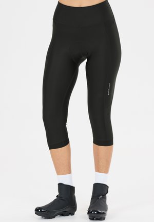 Sorte polstrede cykelcapri tights båret med hvide sokker og sorte cykelskoovertræk, vist på en stående person.