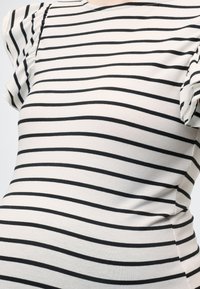 Λευκό και μαύρο οριζόντιο ριγέ κοντομάνικο τοπ με ελαφρώς ραντιρισμένα μανίκια και στρογγυλή λαιμόκοψη σε ένα άτομο.