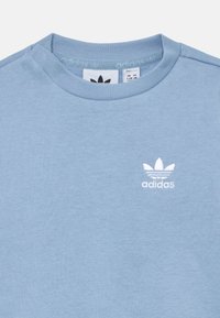 Sweatshirt de gola redonda azul claro, feito de tecido suave. Apresenta um logo da Adidas bordado em branco, com três riscas por cima.