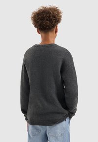 Donkergrijze gebreide trui met een ronde halslijn en lange mouwen. Heeft een zachte textuur en een relaxte pasvorm. Zichtbare stiksel-details bij de zoom.