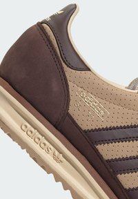Baskets Adidas marron et beige en daim perforé et cuir, avec trois bandes, semelle en caoutchouc texturé et accents en logo doré.