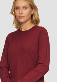 Bordowy, długi sweter z okrągłym dekoltem. Miękka tekstura i dopasowany krój, ukazujący gładkie wykończenie materiału.