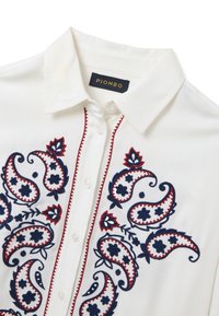 Camicia con colletto bianco caratterizzata da un ricamo paisley intricato in blu navy e rosso sulla parte anteriore, con chiusura a bottoni e cuciture decorative.