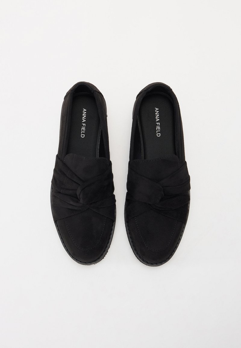 Schwarze Wildleder-Slippers mit Knotendetail an der Oberseite, strukturiertem Oberfläche und flacher Gummisohle. Logo im Inneren des Schuhs.