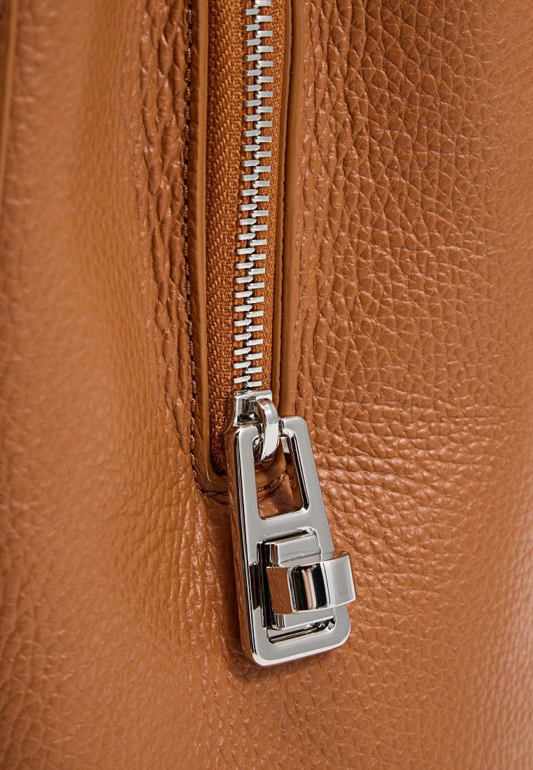 Tasche aus hellem Leder mit einem silbernen Reißverschluss und strukturierten Oberflächen. Der Reißverschluss verläuft vertikal entlang der Tasche und präsentiert metallische Details.
