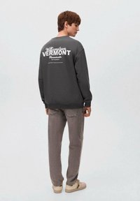 Felpa grigia con la scritta bianca "Williamstown Vermont" sul retro. Abbinata a jeans grigi chiari e sneakers beige, che mostrano un look casual.