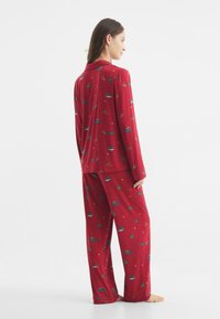 Conjunto de pijama rojo en tejido suave con un estampado de coches coloridos, árboles y estrellas; incluye una parte superior abotonada de manga larga y pantalones de pierna ancha.