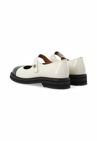 Zapatos de charol blancos con punta negra, que presentan una correa y recortes redondos. Acabado texturizado y una suela negra gruesa.