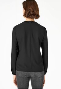 Top nero a maniche lunghe con scollatura arrotondata e rifinitura di perline, texture liscia e cucitura dritta sul retro. Abbinato a jeans grigi.