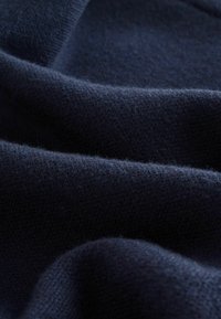 Jūras spēka vilnas audums ar maigu, pūkainu tekstūru, piedāvājot gludas locījumu līnijas un smalkas variācijas, radot bagātu, dziļu krāsas efektu.