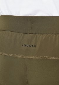 Olijfgroene Aeroready tailleband met zwart logo, gladde textuur en gestikte details. Geen zichtbare patronen of versieringen.