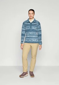 Blå mønstret fleecepullover med krave, lange ærmer og kvart-lynlås. Matchende med beige bukser og brune vandrestøvler.