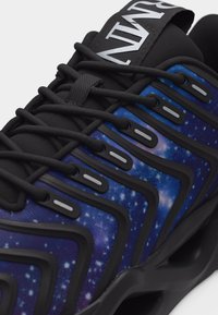 Μαύρο και μπλε αθλητικό παπούτσι με μοτίβο γαλαξία γεμάτο αστέρια, μαύρα κορδόνια και μαύρα επικάλυψη σε ζιγκ-ζαγκ στην επάνω πλευρά.