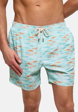 Hombre con pantalones cortos de baño azul claro con un patrón de peces naranja y azul y un cordón blanco.