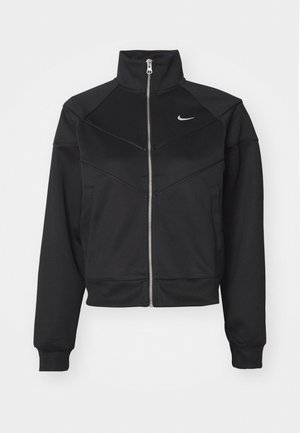 Giacca nera con zip e colletto alto, realizzata in tessuto liscio, con cuciture diagonali e un piccolo logo Nike bianco sul petto.