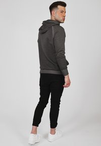 Mörkgrå hoodie i mjukt tyg, med en känguruficka och justerbar dragsko. Matchad med åtsittande svarta byxor och vita sneakers.