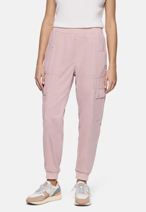 Mujer con pantalones jogger cargo de color rosa claro con puños elásticos y zapatillas blancas con detalles en beige y azul claro.