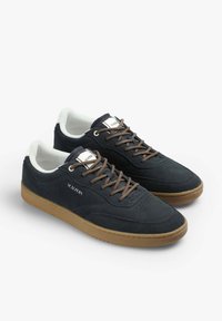 Zapatillas de ante azul oscuro con cordones marrones, cuello blanco, parte superior perforada y suela de goma marrón. Presentan la marca "SCALPERS" en el lateral.