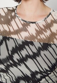 Top trasparente con scollo rotondo, design a strati con motivi astratti beige, marrone e nero, e rifinitura metallica lungo il colletto.