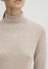 Bežna, prilagođena turtleneck majica napravljena od mekog materijala s rebrastom teksturom na ovratniku i manžetama, dizajnirana za usku siluetu.