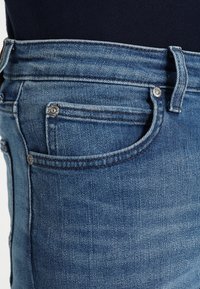 Blue denim jeans with a straight cut, featuring a button closure, two front pockets, and faded texture on the waistband and side.