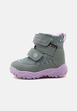 Botte d'hiver enfant verte et violette avec motifs de flocons de neige, deux sangles réglables, semelle épaisse à crampons et étiquette imperméable Gore-Tex.