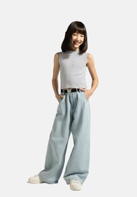 Szara i biała pasiasta bluzka bez rękawów, jasnoniebieskie szerokie dżinsy, czarny pasek z srebrną klamrą i białe sneakersy. Ręce w kieszeniach.