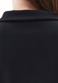 Top de algodón negro con una textura suave, que presenta un cuello redondeado y un diseño limpio y minimalista. Sin patrones ni acentos visibles.