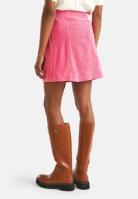 Woman wearing a pink corduroy skirt and tall brown leather boots, shown from the back against a plain background.