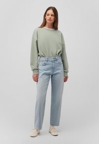 Felpa verde chiaro con spalle scese, abbinata a jeans a vita alta azzurri e larghi. Sneakers in colore neutro completano il look.