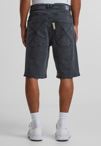 Dunkelgraue Denim-Shorts mit geradem Schnitt, sichtbaren Nähten und zwei Gesäßtaschen. Etikett an der rechten Tasche, gesäumte Kanten.