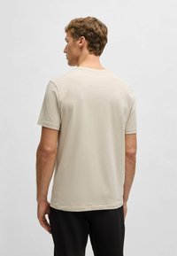 Camiseta de color beige claro con mangas cortas, escote redondo y textura de algodón suave. Presenta un detalle de costura mínima en la parte posterior.