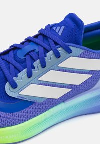 Baskets de course bleues avec un dessus en maille, design à trois bandes blanches et une semelle dégradée de vert à bleu. Comprend une languette rembourrée et des lacets texturés.