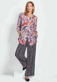 Lichte, kleurrijke blouse met knopen en een bloemenpatroon, gecombineerd met wijde zwarte en witte gestreepte broek. Zwarte flats maken de outfit compleet.