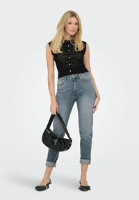 Haut noir sans manches en tricot avec un motif en dentelle, associé à un jean bleu clair et un sac noir. Les accessoires comprennent des chaussures à talons avec un détail en nœud.