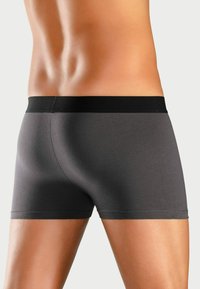 Graue Boxershorts mit einem schwarzen elastischen Bund, die ein glattes, eng anliegendes Design aufweisen, das die Form des Körpers betont.