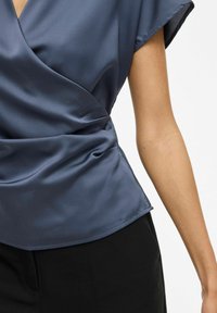 Haut en satin bleu marine à manches courtes, avec une taille cintrée et une texture lisse. Pantalons noirs visibles en bas.