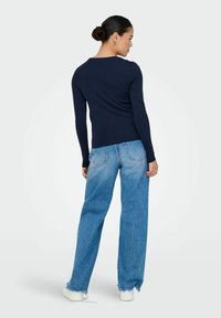 Top de manga larga azul marino combinado con unos vaqueros de tiro alto en azul claro, con un corte relajado y dobladillos deshilachados. Modelo de espaldas.