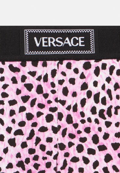Ceinture élastique noire avec le logo blanc "VERSACE" au-dessus d'un tissu rose côtelé orné de taches de léopard noires.