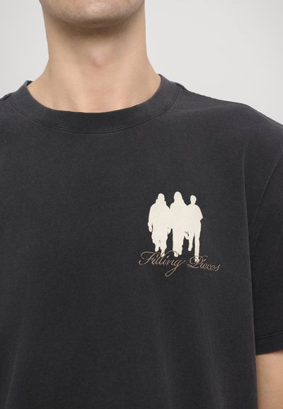 Black cotton t-shirt featuring a printed design of three figures in white and the text "Filling Pieces" in cursive below.
