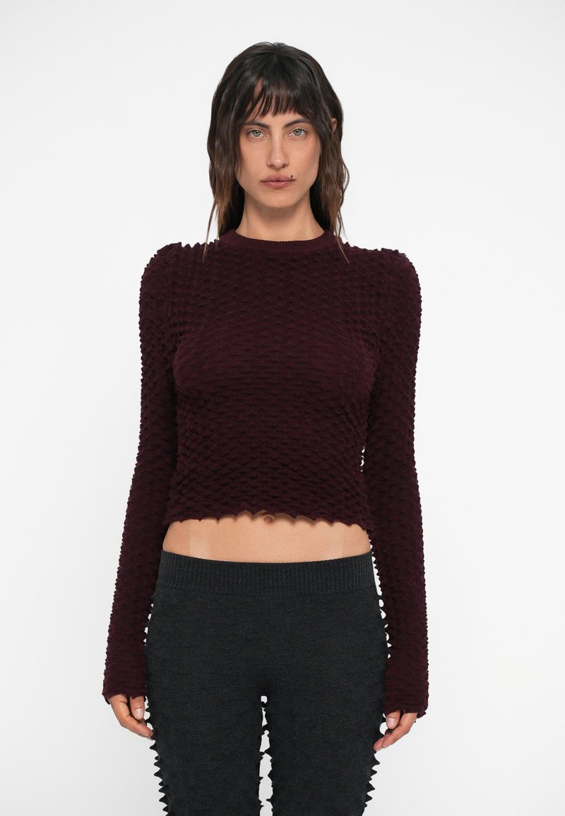 Burgundy színű, texturált crop top hosszú ujjal, fodros aljjal, sötét, bordázott, magas derekú nadrággal párosítva, szintén texturált.