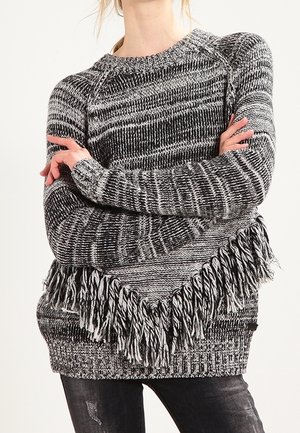 Black and white knitted sweater with fringe detailing at the hem, featuring a textured pattern and raglan sleeves.
