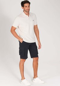 Polo shirt gris clair à manches courtes, associé à un short cargo foncé et des baskets blanches. Le short cargo possède des poches latérales et une coupe droite.